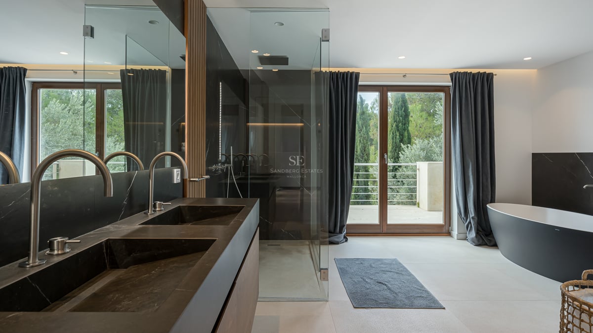 Salle de bains moderne avec double vasque noire, douche à l'italienne, baignoire îlot et vue sur la forêt.