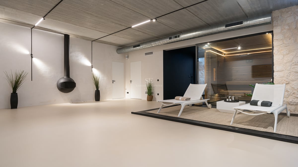 Minimalistiskt inomhus-spa med inglasad bastu, vit solstol och industriell inredning.