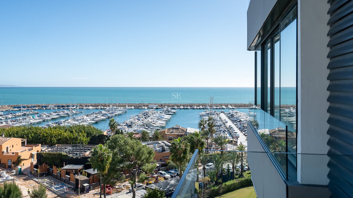 Erhöhte Ansicht von einem modernen Balkon über einen Yachthafen und das Mittelmeer unter klarem blauem Himmel.