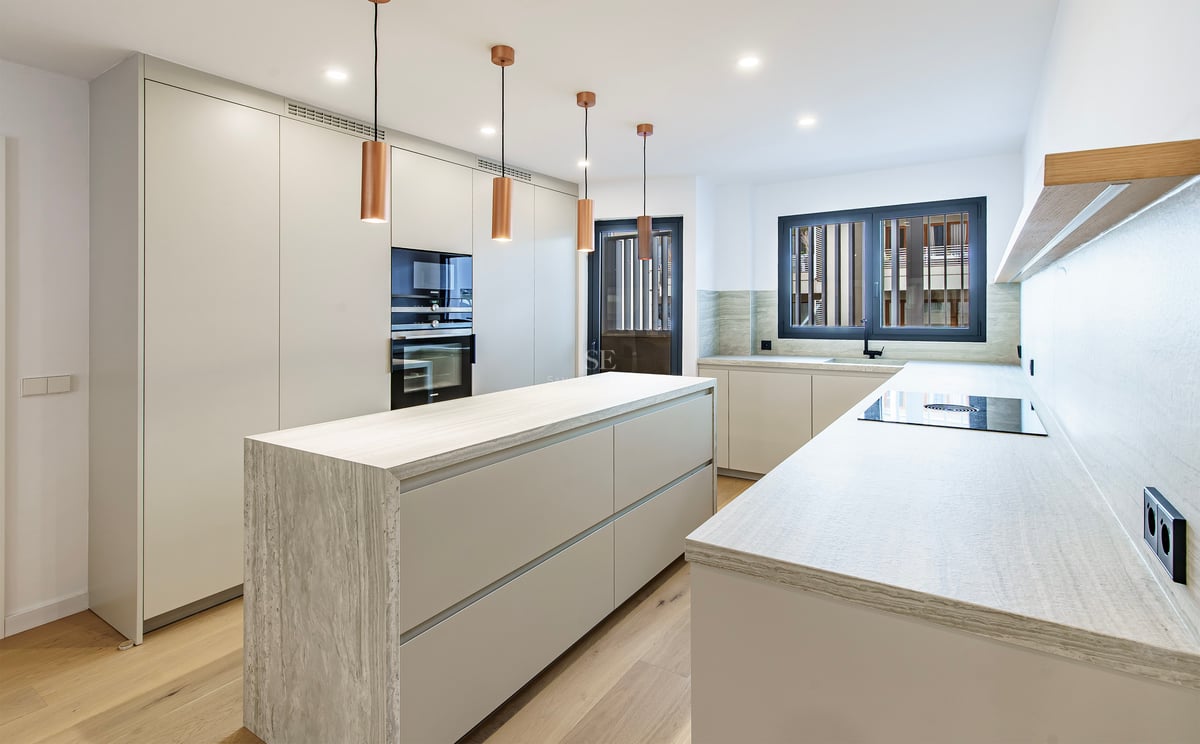 Cuisine contemporaine blanche avec îlot en pierre, suspensions en cuivre et parquet en bois.