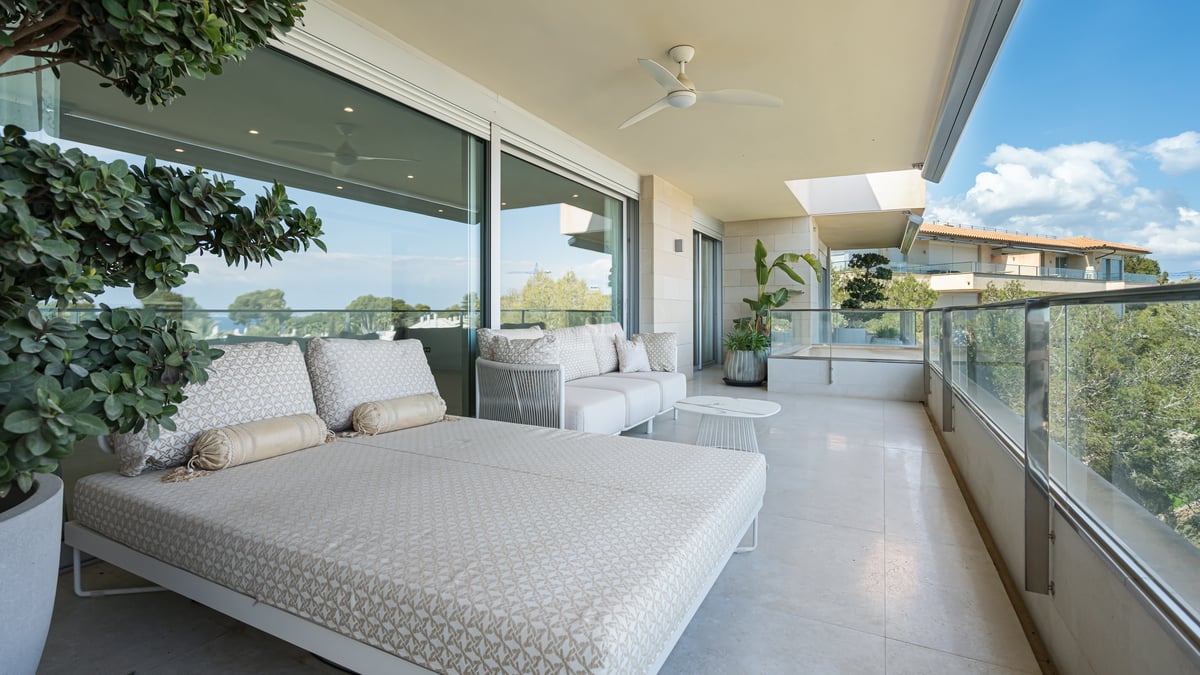 Large covered terrace with patterned daybed, glass railings, and views of lush greenery.