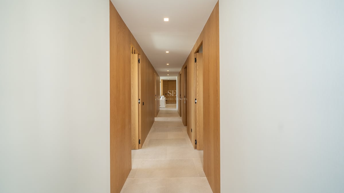 Couloir symétrique avec panneaux muraux en chêne clair, sol en pierre naturelle et éclairage encastré au plafond.