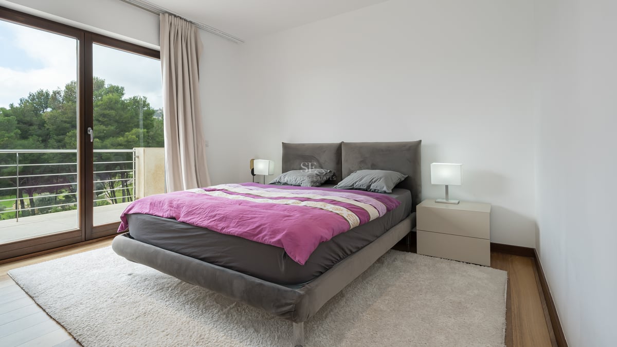 Chambre contemporaine avec lit rembourré gris, couette prune, tapis blanc et porte-fenêtre donnant sur un balcon.