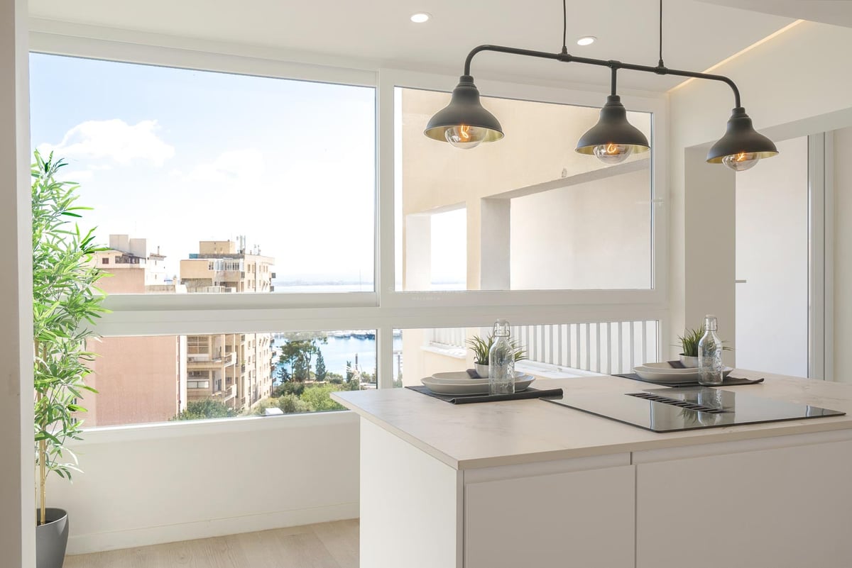 Weiße Kücheninsel mit Induktionskochfeld vor einem großen Fenster mit Blick auf den Hafen und die Stadt.