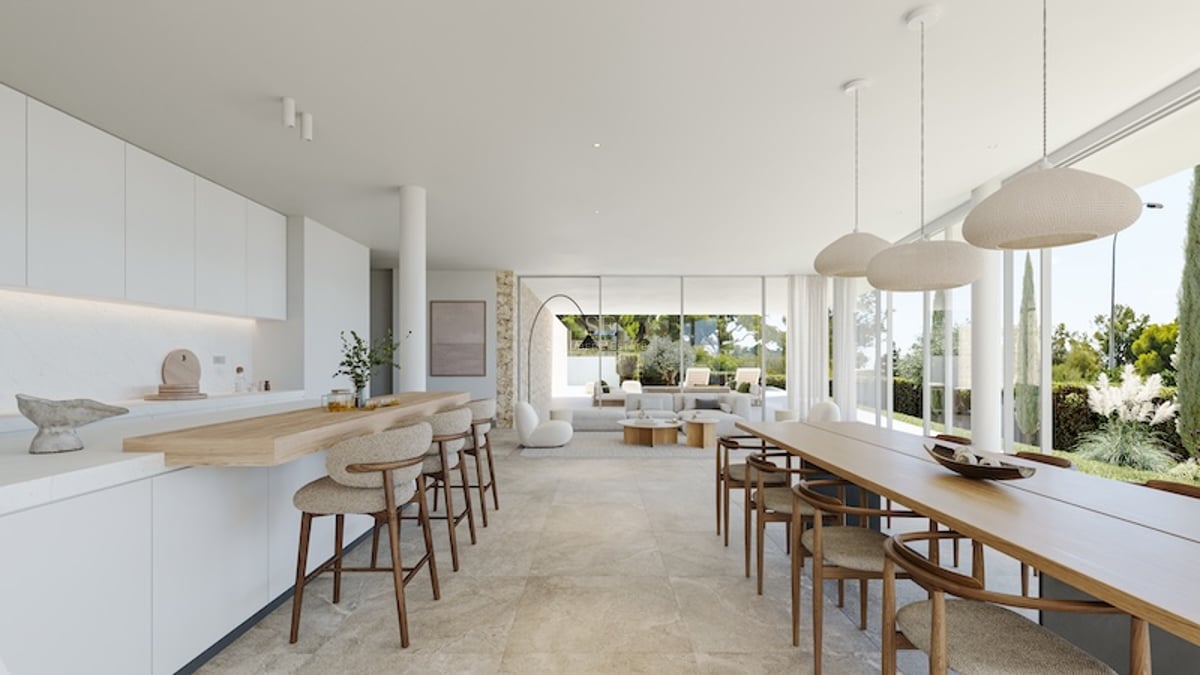 Vue grand-angle d'une cuisine blanche minimaliste et d'un coin repas avec de grandes baies vitrées sur un jardin.