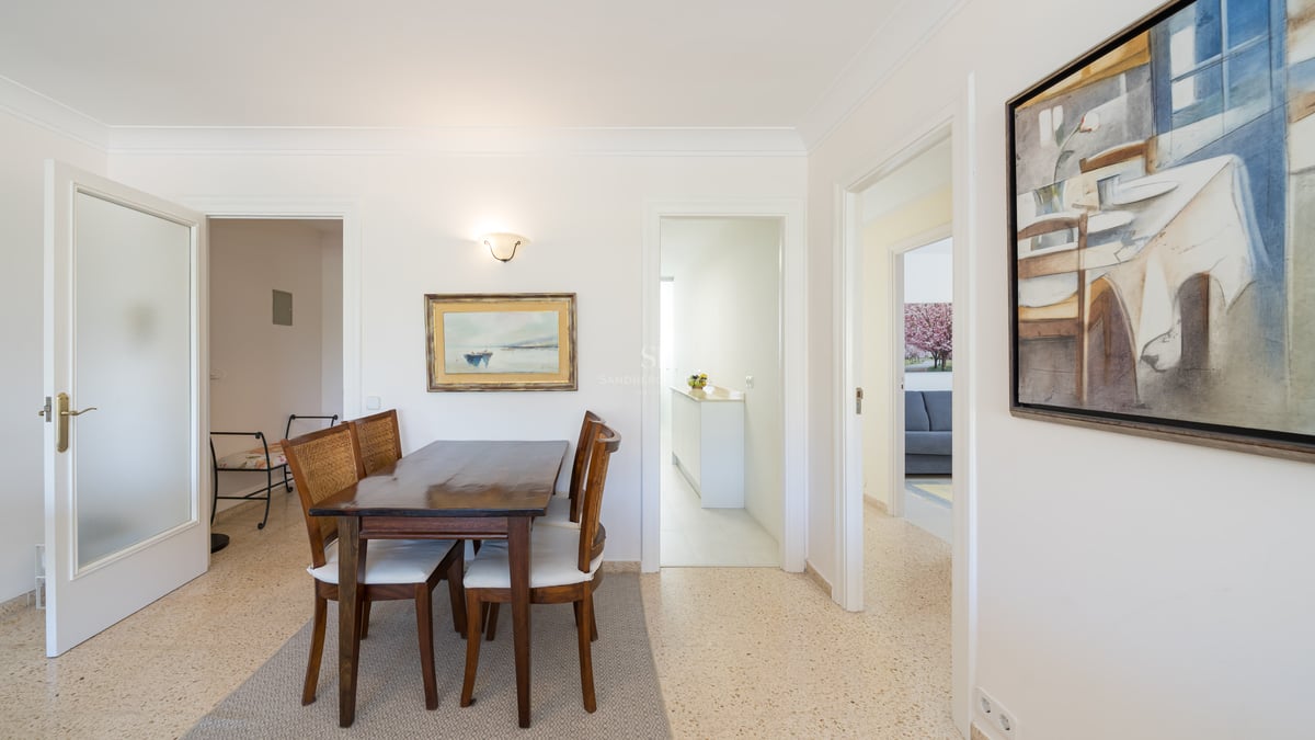 A dark wood dining table and four chairs with woven backs and white cushions in a bright, white room.