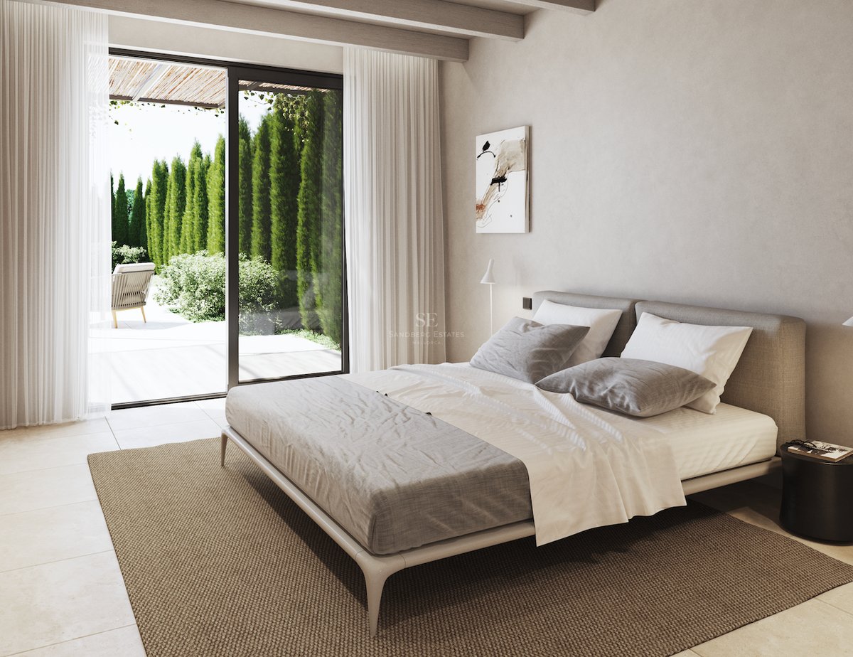 Chambre contemporaine avec poutres en bois, grand lit et baies vitrées ouvrant sur un jardin ensoleillé.