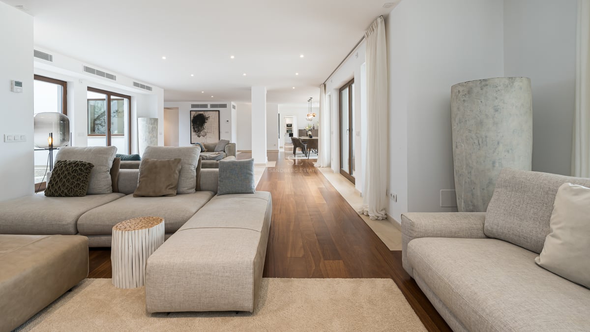 Salon moderne spacieux avec canapés en tissu gris, parquet en bois foncé et baies vitrées.