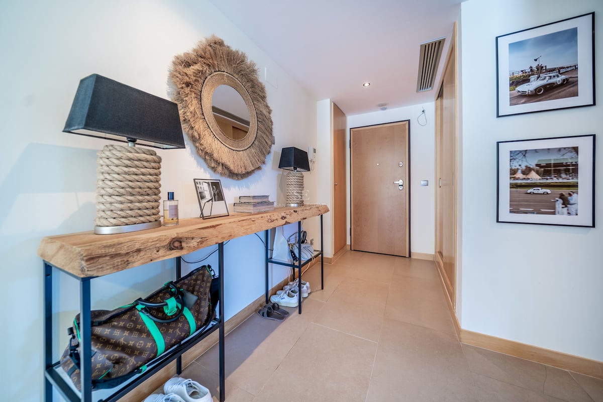 Couloir d'entrée moderne avec console en bois brut, miroir en jute et carrelage beige chaleureux.