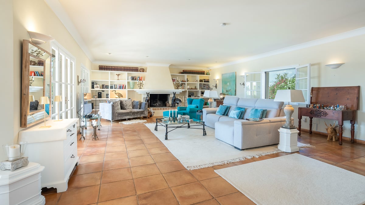 Grand salon avec sol en terre cuite, une grande cheminée blanche et des étagères de bibliothèque intégrées.