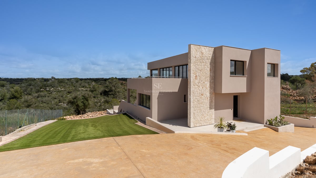 Moderne zweistöckige Villa mit sandfarbener Fassade, Natursteinakzenten und großen Fenstern mit Blick auf den Rasen.