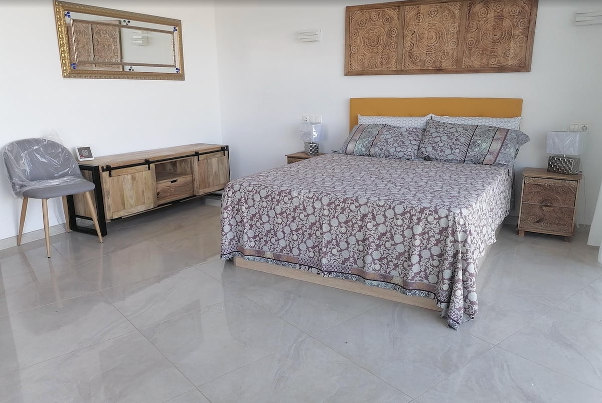 Chambre avec lit double, tête de lit en bois sculpté, sol en marbre poli et lumière naturelle.