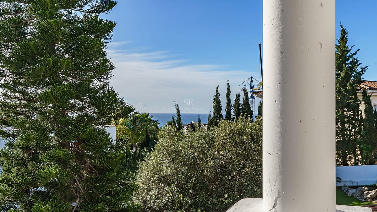 Utsikt över Medelhavet inramad av en vit pelare och frodig grönska under en blå himmel.