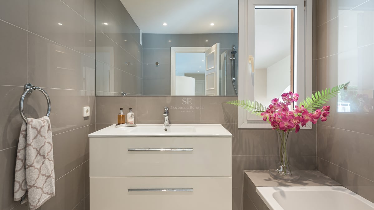 Contemporary bathroom featuring a white vanity, integrated sink, large mirror, and taupe wall tiles with chrome accents.