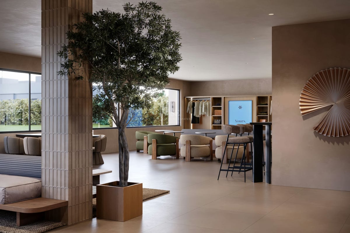 Hall moderne avec un arbre d'intérieur, des fauteuils vert olive, des piliers carrelés et de grandes fenêtres.