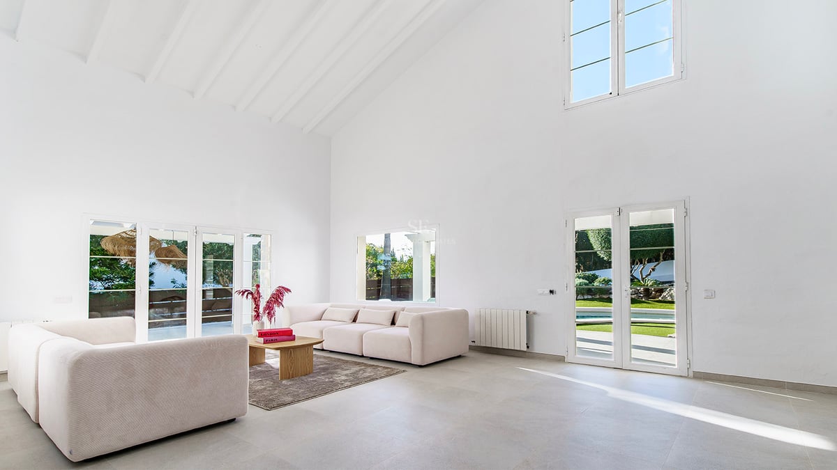 Rymligt vardagsrum med vita ryggåstak, beige soffor och altandörrar som leder ut till trädgården.