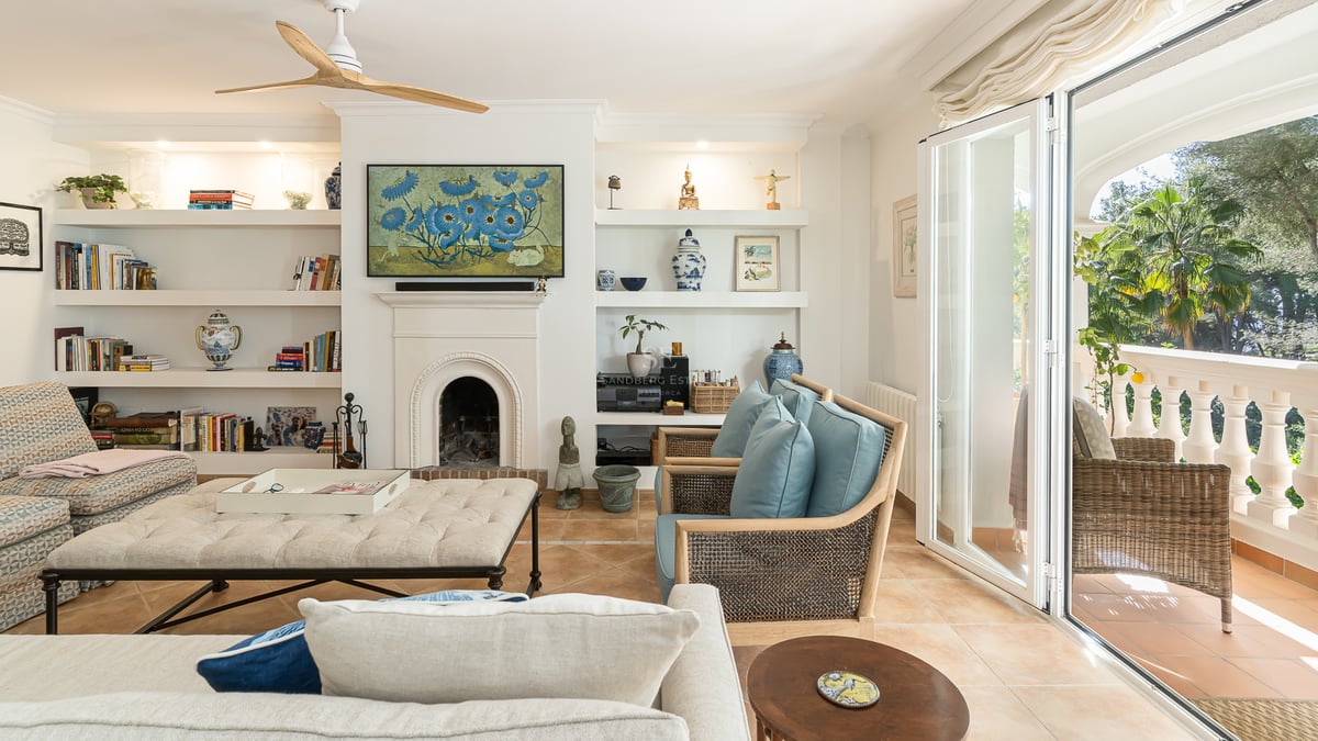 Bright living room with terracotta floors, white fireplace, built-in shelves, and glass doors opening to a lush terrace.