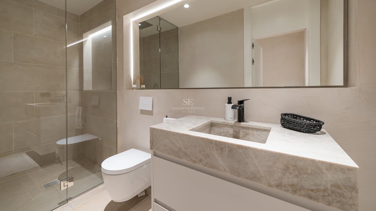 Salle de bains moderne avec vasque en marbre, miroir rétroéclairé, WC suspendu et douche à l'italienne en verre.