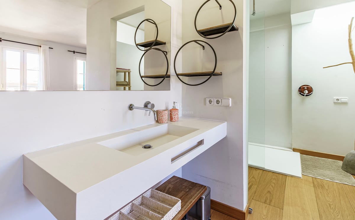 Modernt vitt badrum med stort integrerat handfat, runda vägghyllor och en duschkabin i glas.