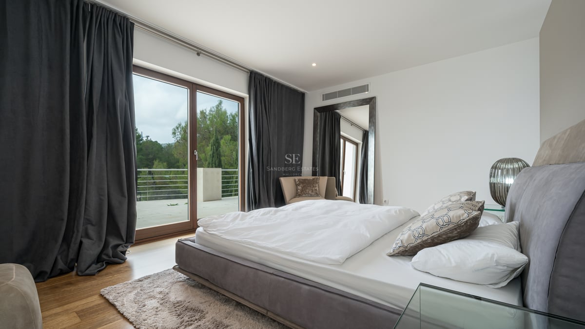 Chambre principale contemporaine avec literie blanche, rideaux anthracite et baies vitrées ouvrant sur une terrasse.