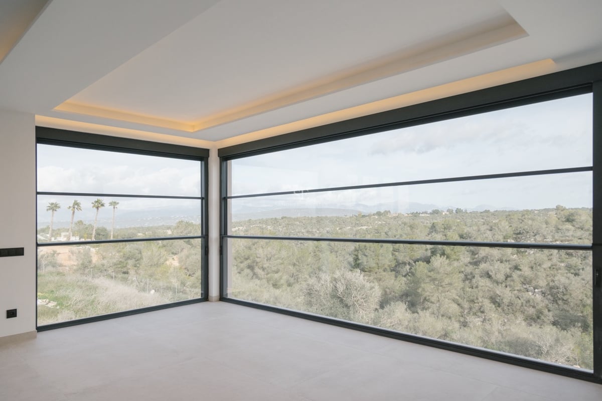 Moderner leerer Raum mit bodentiefen Eckfenstern und Blick auf eine üppige grüne Landschaft und ferne Berge.