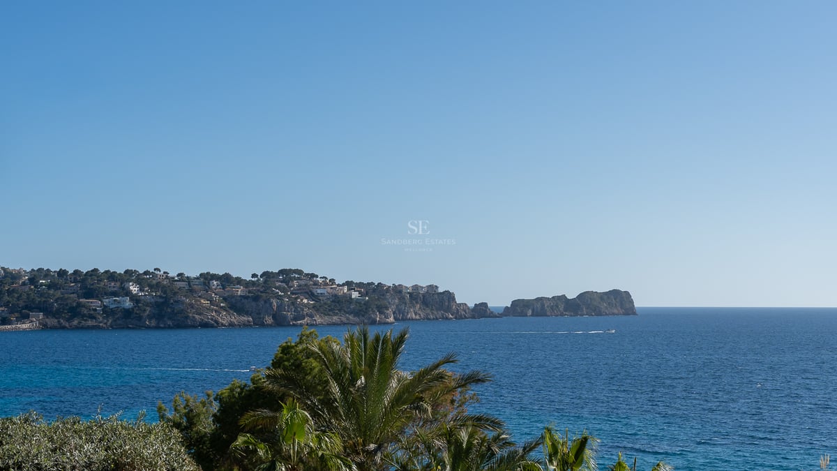 Weitwinkelblick auf das Mittelmeer mit Klippen, Luxusvillen und Palmen unter einem klaren blauen Himmel.