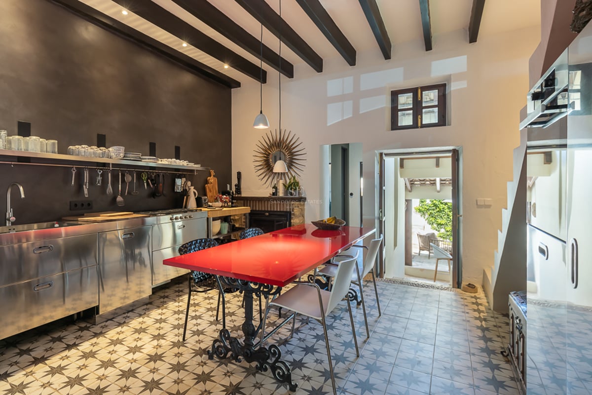 Cuisine moderne avec placards en inox, table rouge et carrelage hydraulique traditionnel.