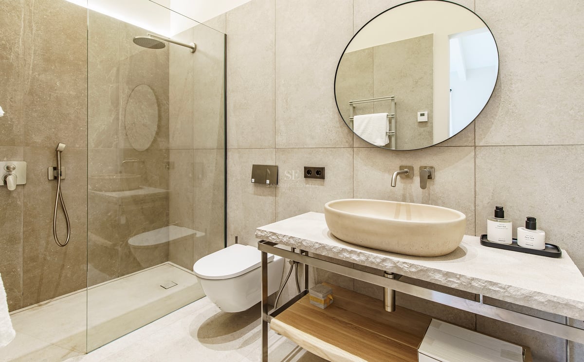 Zeitgenössisches Badezimmer mit Stein-Aufsatzwaschbecken, rundem Spiegel und begehbarer Glasdusche.