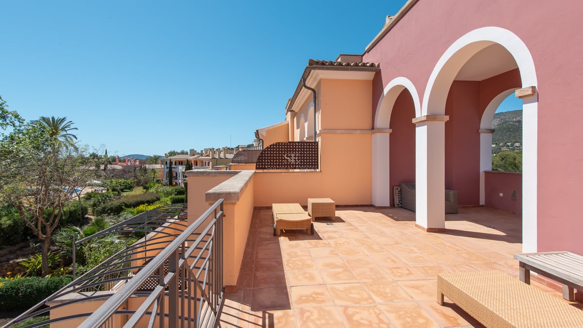 Sunny terracotta terrace with arches, sun loungers, and views of lush gardens and hills under a clear blue sky.
