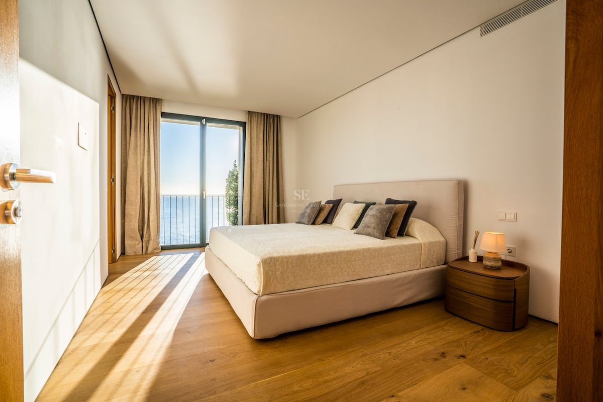 Modernes Schlafzimmer mit Eichenparkett und bodentiefen Glastüren, die den Blick auf das Mittelmeer freigeben.