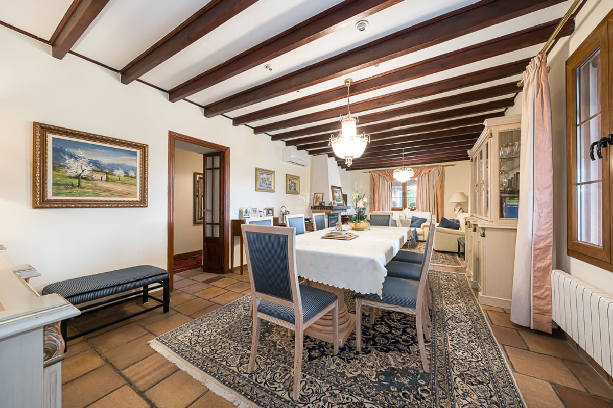 Salle à manger formelle avec poutres en bois sombre, sol en terre cuite et grande table sous un lustre classique.