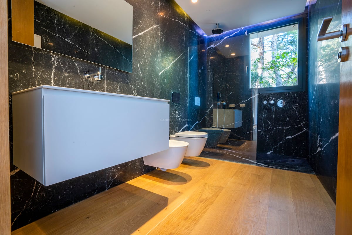 Modernes Bad mit schwarzen Marmorwänden, Eichenboden, weißem Waschtisch und verglaster Dusche.