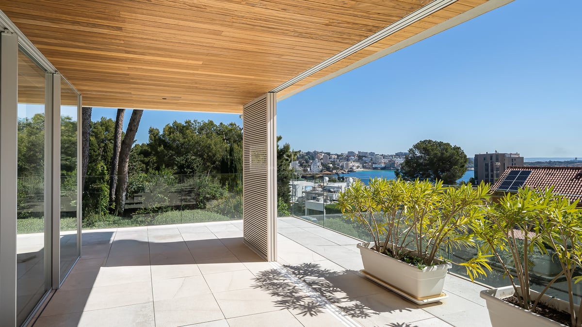 Moderne Terrasse mit hochwertiger Holzdecke, Glasgeländer und weitem Blick auf die Küstenbucht.
