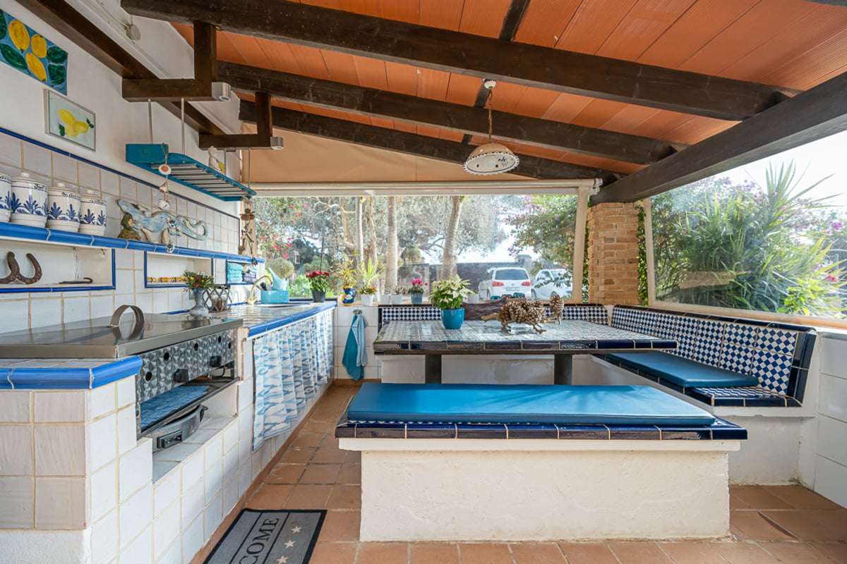 Terrasse couverte avec cuisine d'été en carreaux bleus et blancs, bancs intégrés et plafond à poutres en bois.