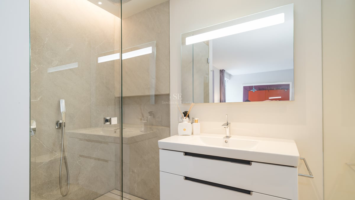 Modernes Badezimmer mit weißem Waschtisch, großem LED-Spiegel und rahmenloser Glasduschwand.