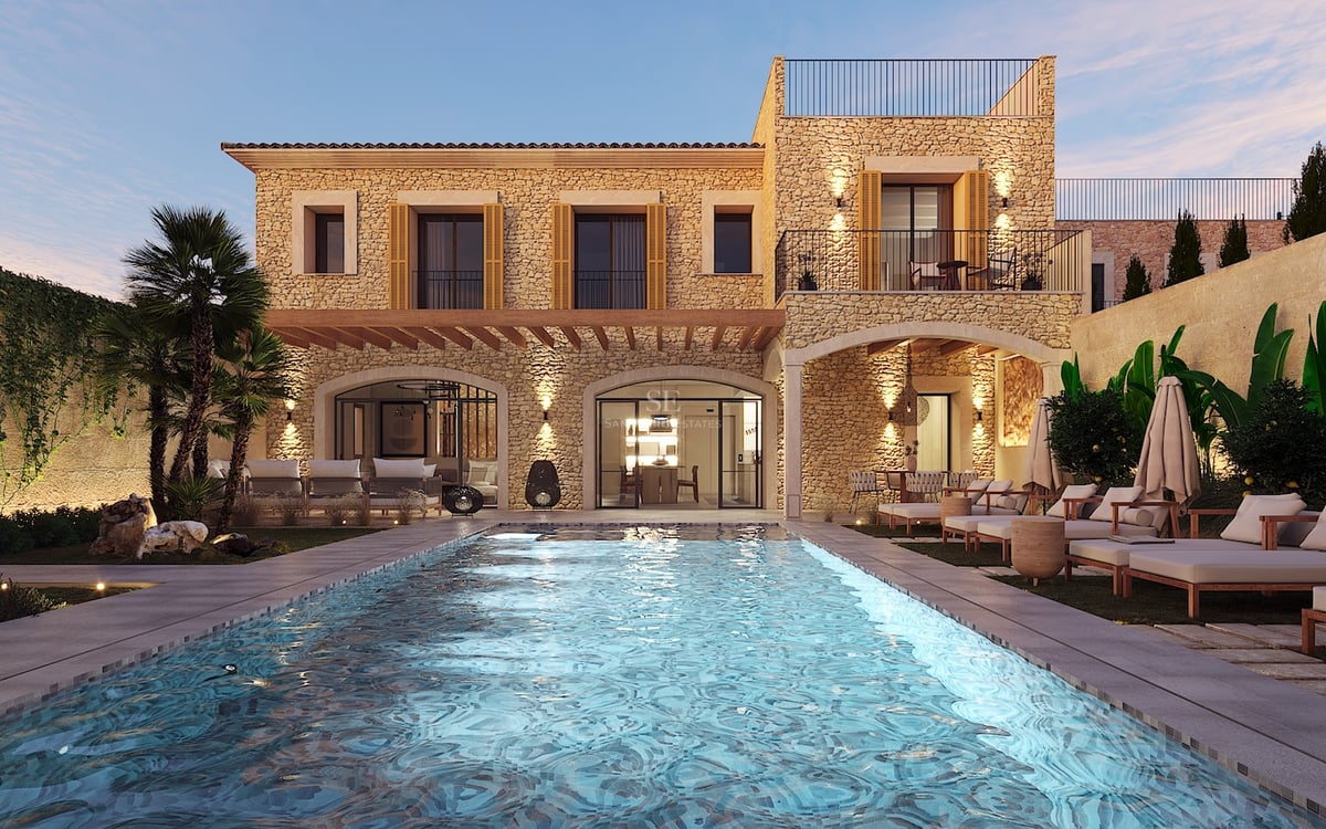 Vue nocturne d'une villa en pierre avec piscine éclairée, bains de soleil et palmiers sous un ciel de crépuscule.