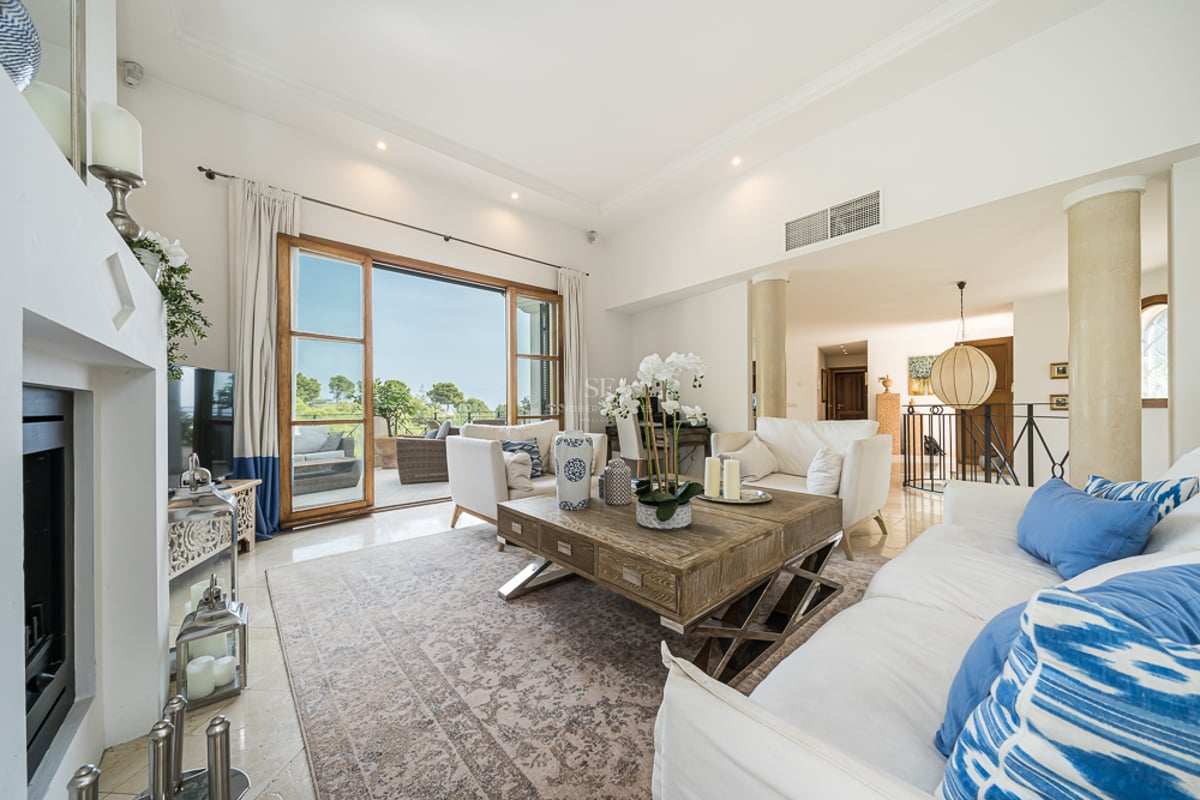 Ljust vardagsrum med vita soffor, ett rejält soffbord i trä och skjutdörrar i glas mot en terrass.