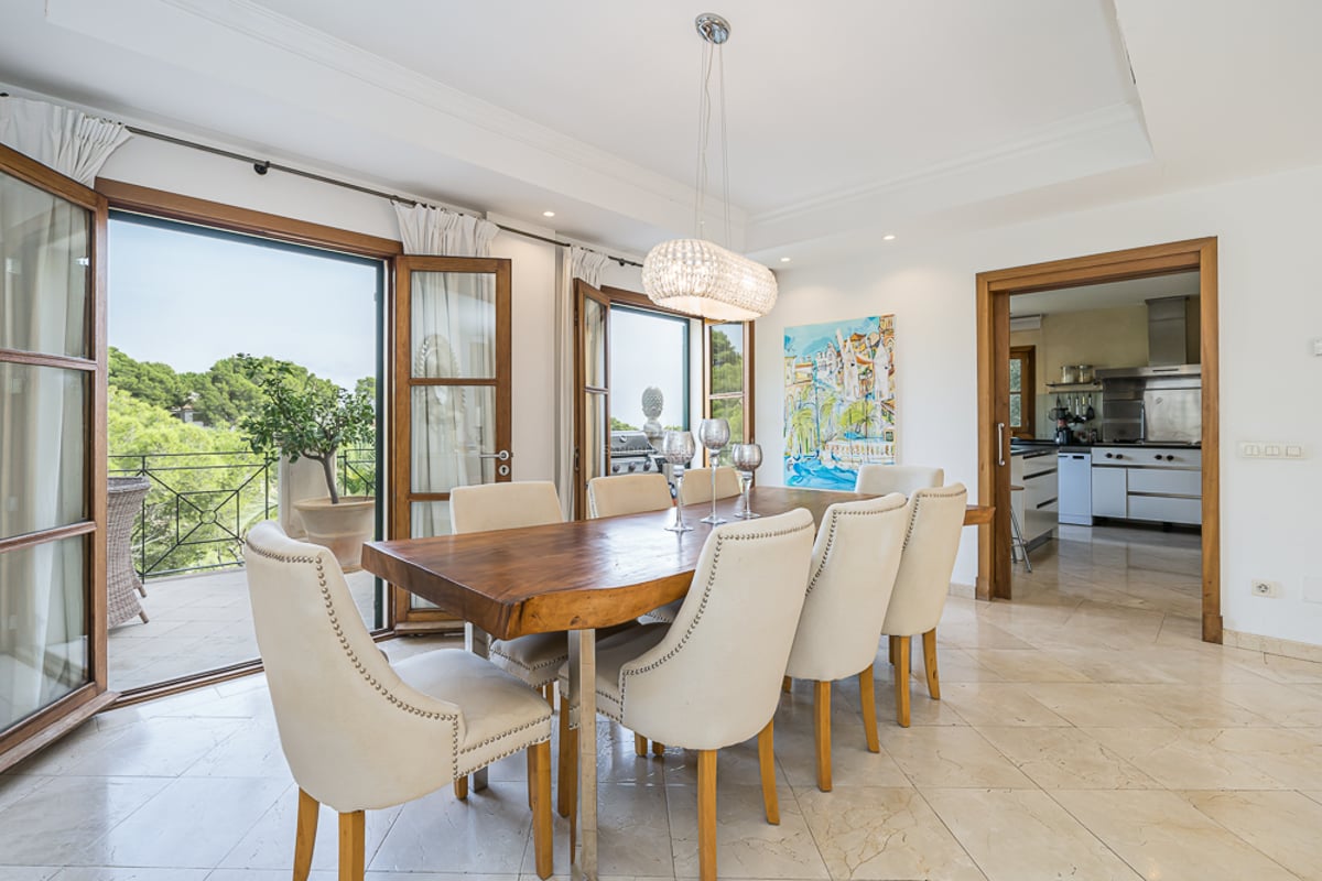 Matsal med ett massivt träbord, krämvita stolar och stora glasdörrar som leder ut till en balkong.