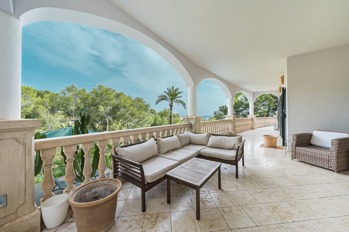 Rymlig terrass med valv, utemöbler, stenbalustrader och utsikt över prunkande grönska och havet.