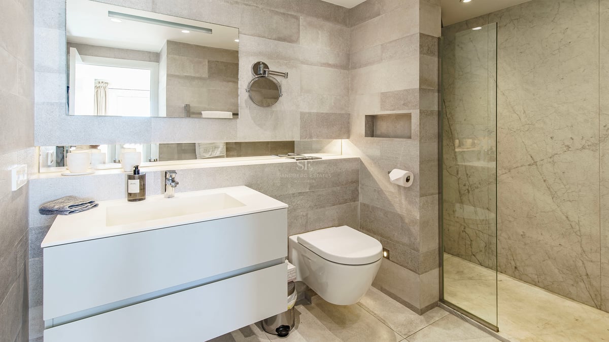 Minimalist bathroom featuring grey stone walls, white floating vanity, and a glass walk-in shower.