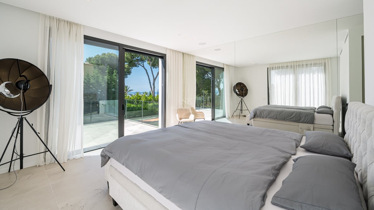 Chambre moderne avec grand lit, baies vitrées et terrasse privée offrant une vue sur les pins et la mer.