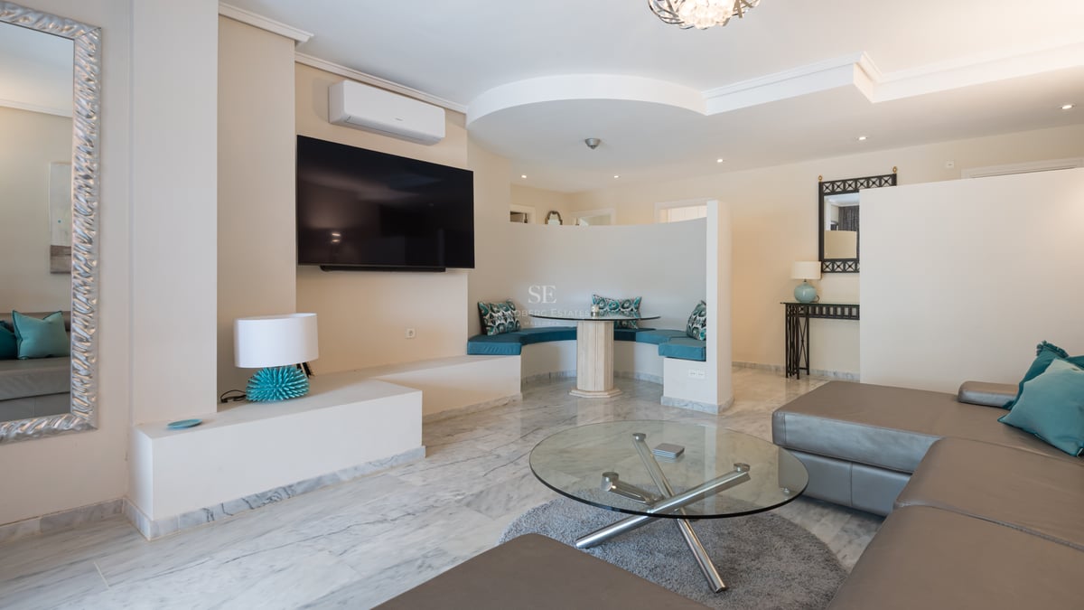 Modern living room featuring marble floors, a large TV, leather sofa, and a curved breakfast nook with turquoise cushions.