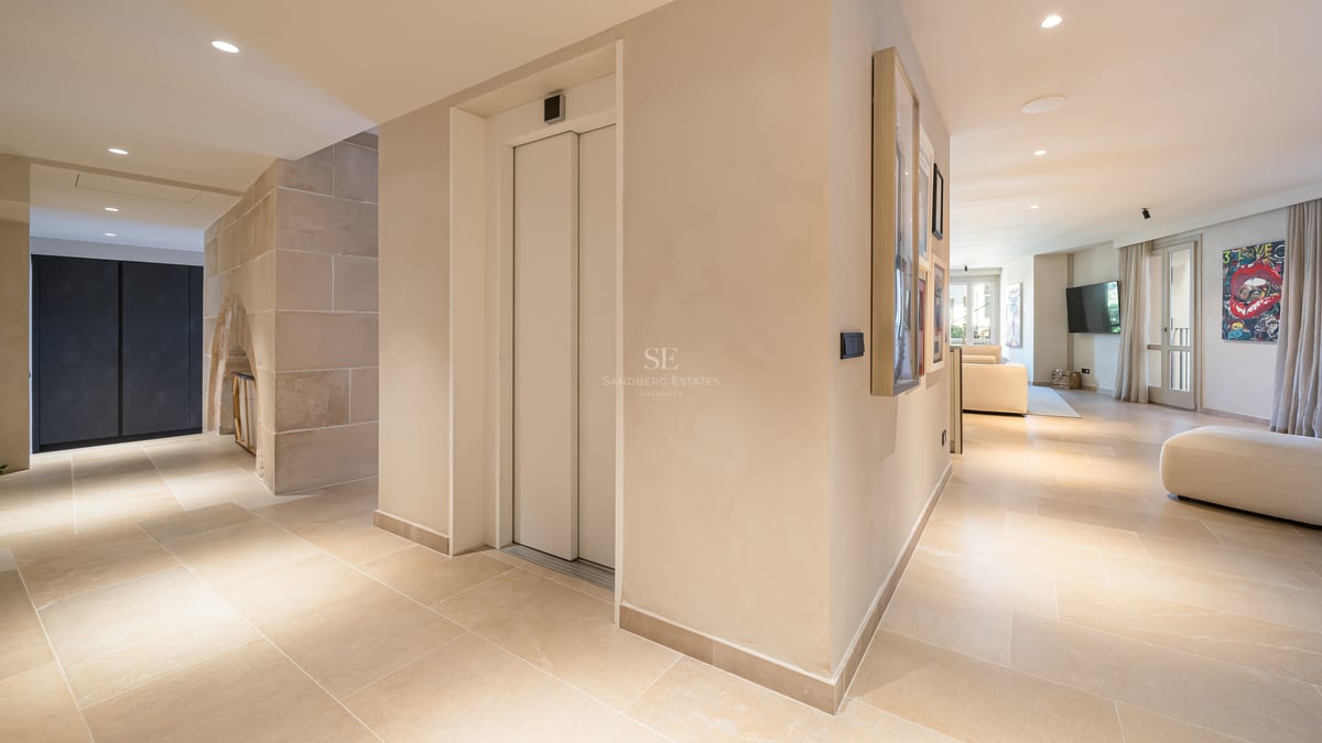 Couloir intérieur moderne avec ascenseur privé blanc, sol en pierre naturelle et éclairage encastré chaleureux.