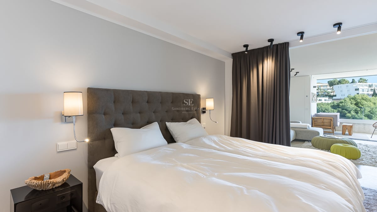 Modernes Hauptschlafzimmer mit grauem gestepptem Kopfteil, weißer Bettwäsche und Glastüren zum Balkon.