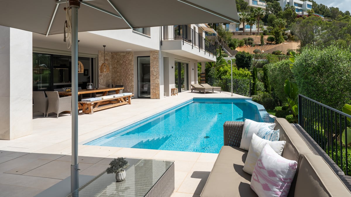 Vue panoramique de piscine à débordement, entourée de végétation et d'architecture moderne. Lumière naturelle et ambiance sereine.