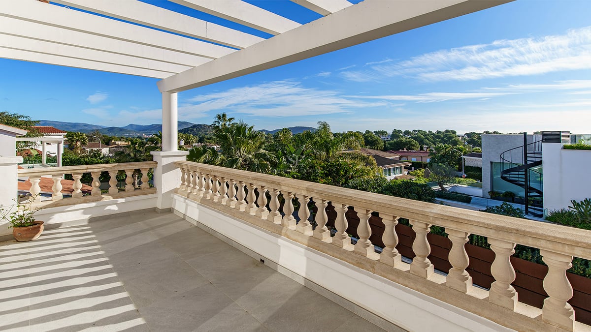 Upphöjd terrass med vit pergola, klassisk stenbalustrad och panoramautsikt över grönska och berg.