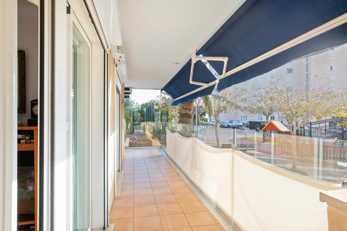 Langer Balkon mit Terrakottafliesen, Glasgeländer und blauen Markisen mit Blick auf die Wohngegend.