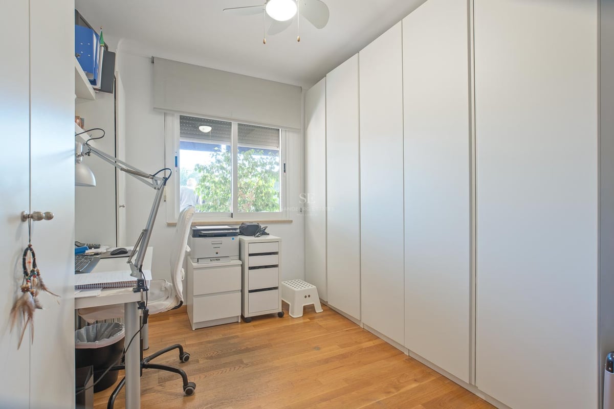 Heller Raum mit deckenhohen weißen Einbauschränken, Holzboden und einem Schreibtisch am Fenster.