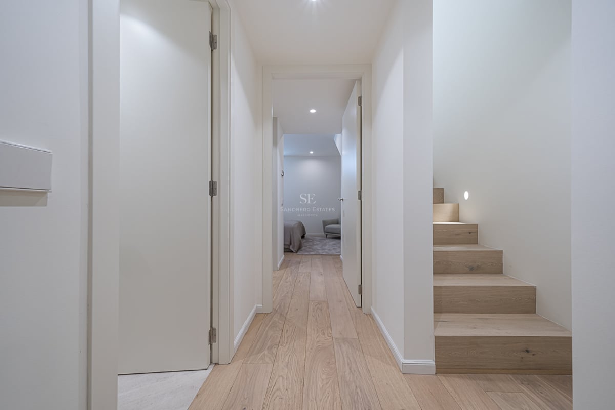 Bright modern hallway with light wood floors, white walls, and a wooden staircase with integrated wall lighting.