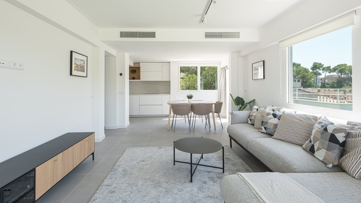 Salon lumineux avec canapé gris, coin repas et cuisine blanche épurée avec vue sur la nature.